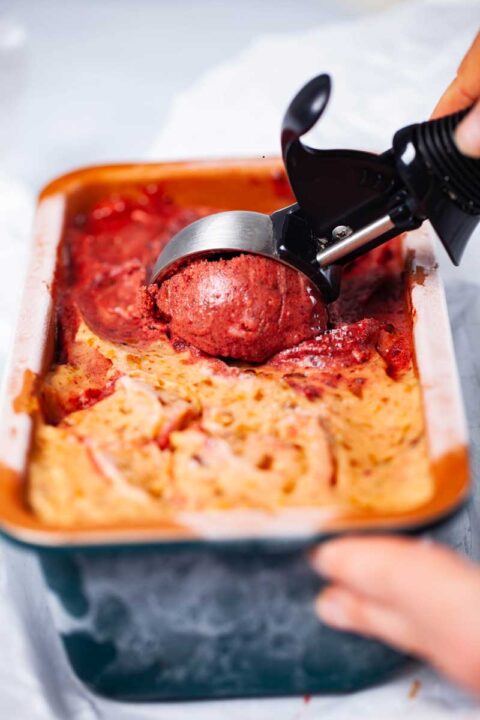 A hand holding a ice cream container while scooping up a bowl of two-flavored ice cream with the other hand.