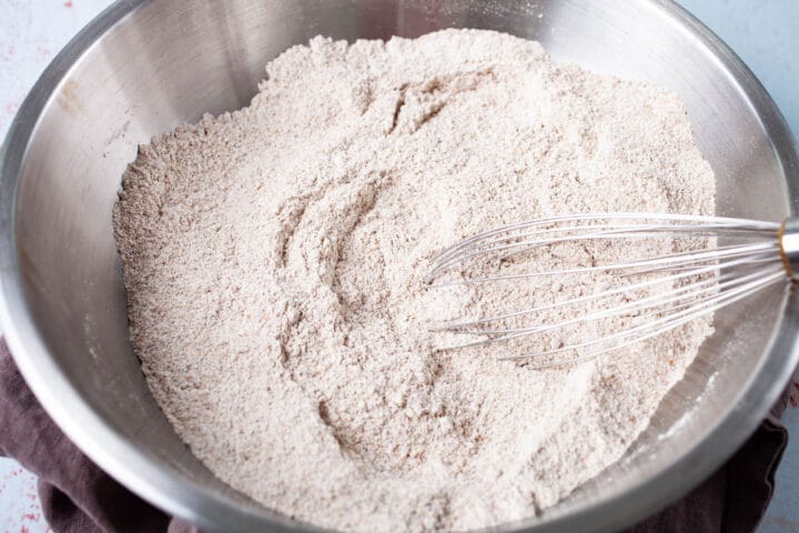 A whisk resting in a bowl of sifted flour.