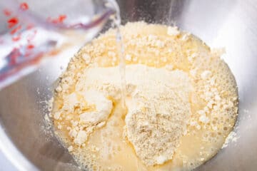 Someone adding water to flour in a stainless steel bowl.