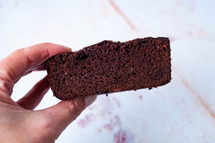 A hand holding a piece of a low carb loaf cake.