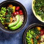 Bowls filled with cooked rice, small tomatoes, avocado slices, fried edamame beans, fried plantains, and topped with chimichurri sauce.