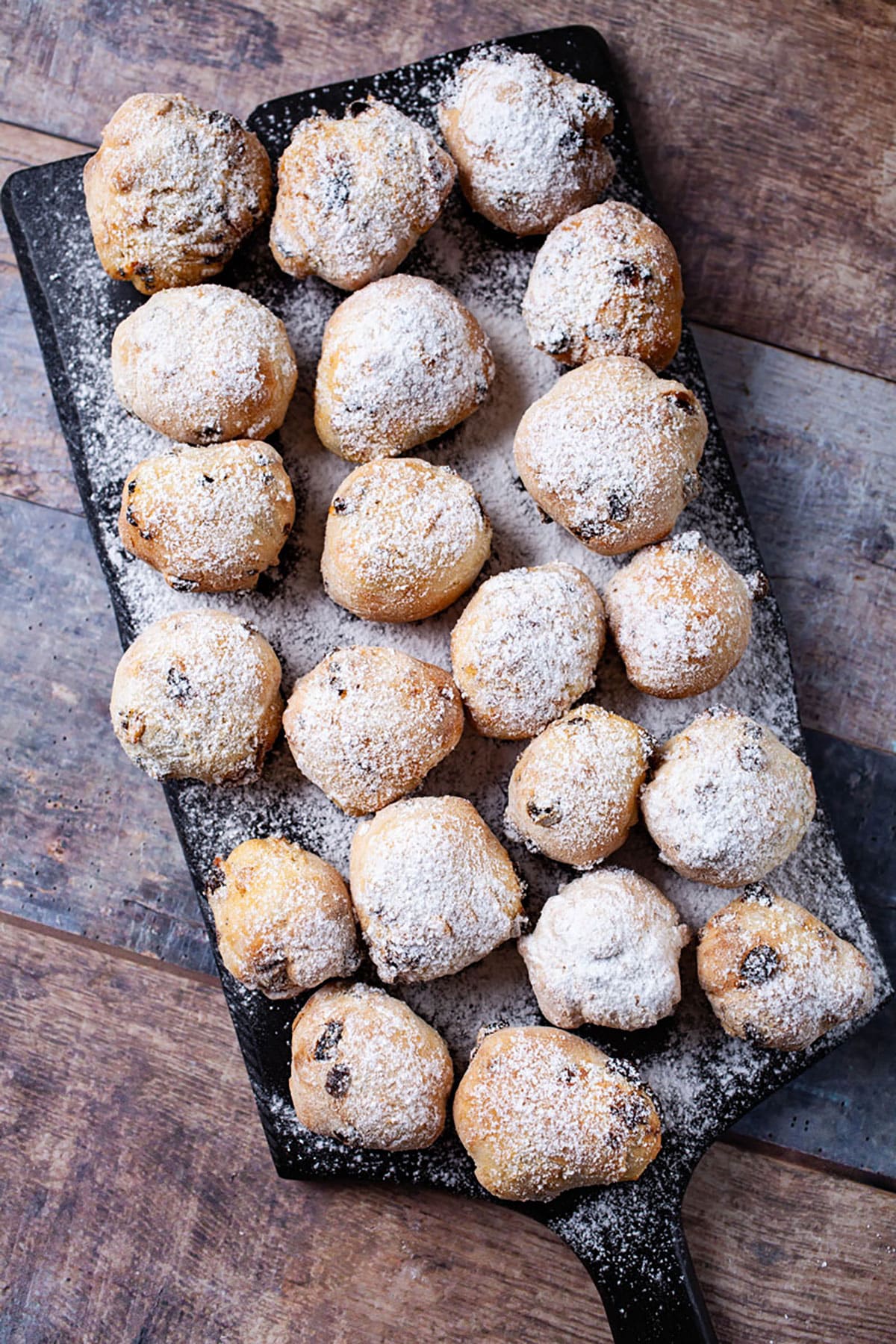 A wooden board filled with air fried and raisin filled doughnuts.