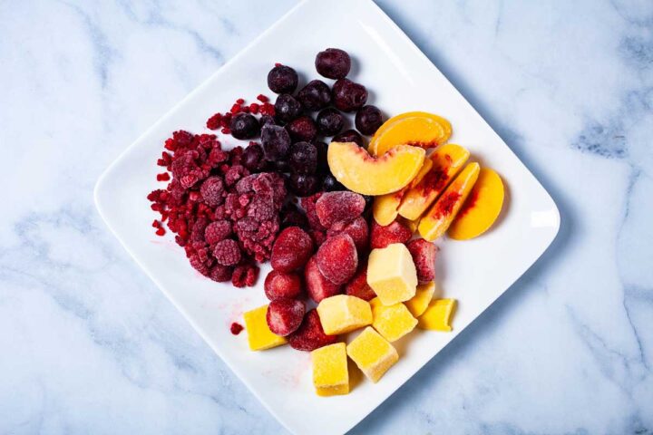 A plate with an assortment of frozen fruits like raspberries, dark cherries, strawberries, peaches, and mango.