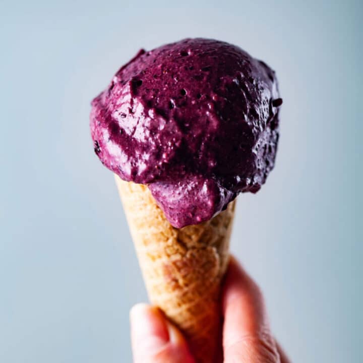 A hand holding a creamy berry ice cream in a cone.