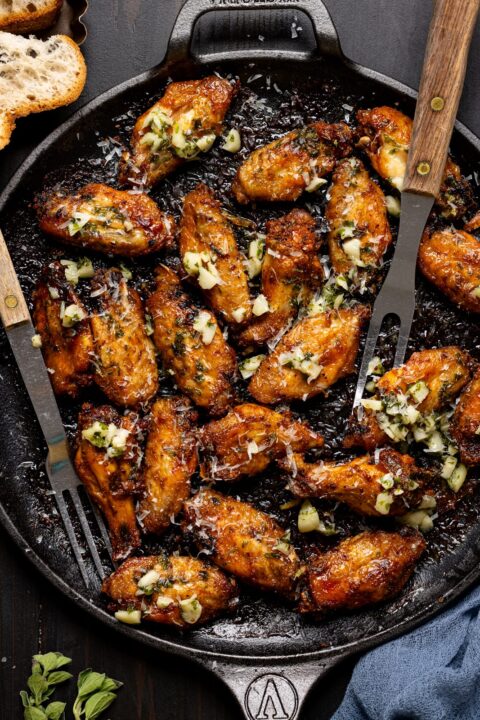 an overhead shot of garlic parmesan chicken whites in a cast iron skillet with grilling utensils tucked in the side of the skillet.