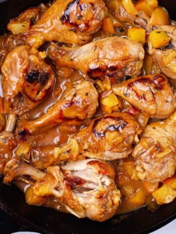 A cast iron skillet with glazed peach chicken legs.