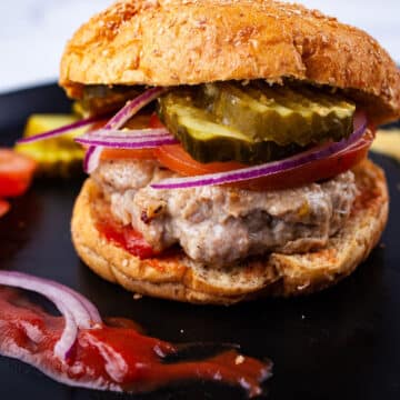 Gluten free turkey burger topped with slices of tomato, thinly sliced red onions, pickles in a bun next to a dollop of ketchup.