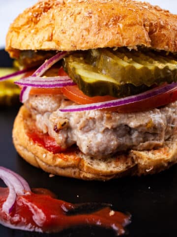 Gluten free turkey burger topped with slices of tomato, thinly sliced red onions, pickles in a bun next to a dollop of ketchup.