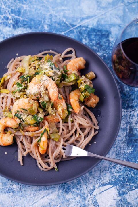 Garlic shrimp and cassava flour pasta served on a plate next to a glass of red wine.