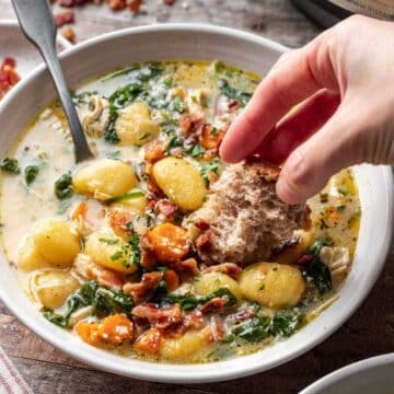 Someone dipping a piece of bread in a bowl of gnocchi soup.