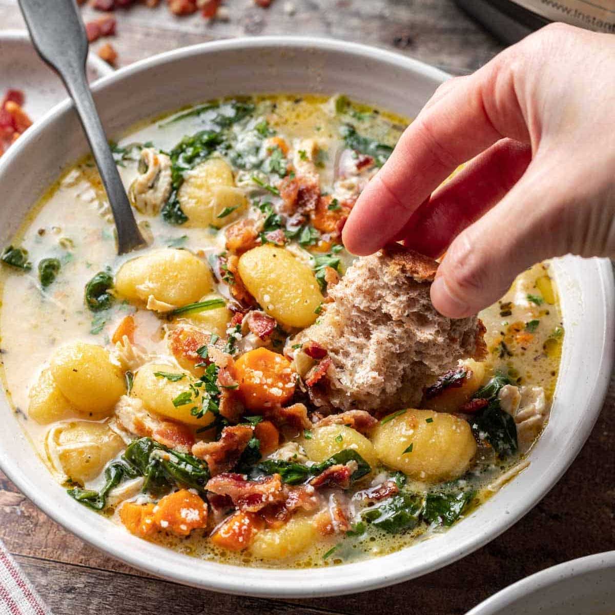 Someone dipping a piece of bread in a bowl of gnocchi soup.
