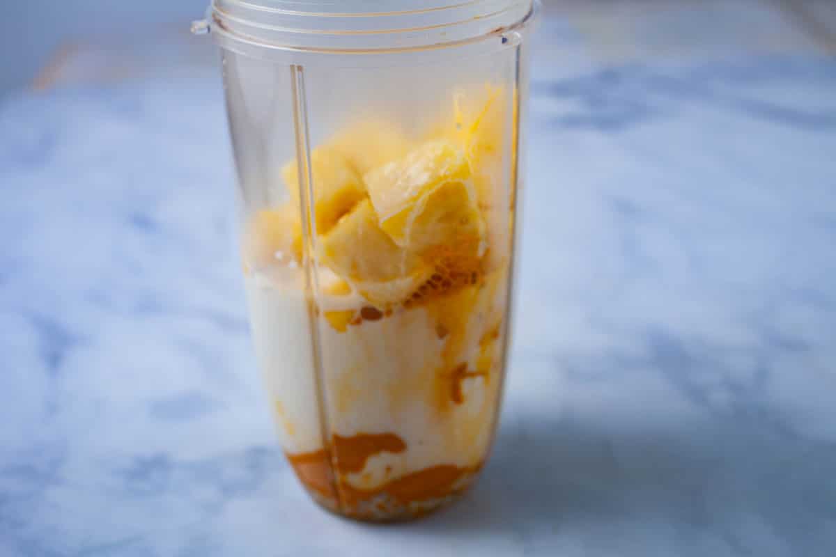 Turmeric, milk, and fruits stacked in a blender.
