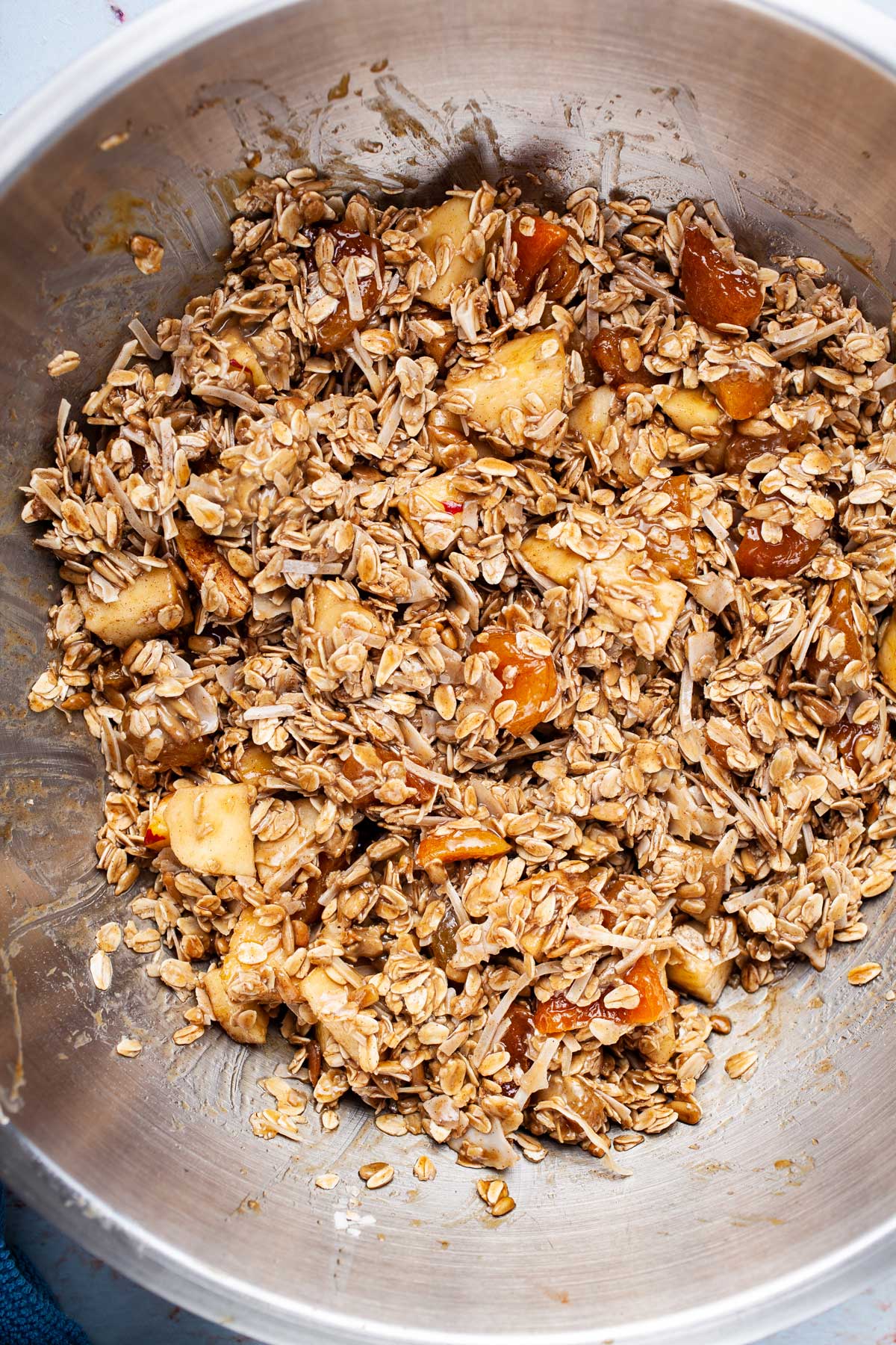 A sticky oats and seeds mixture with apples and dried fruits in a large mixing bowl.