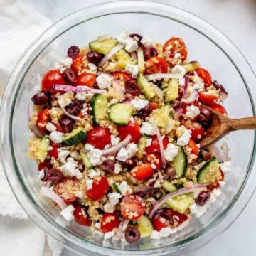 Cooked quinoa, cucumbers, onions, mini tomatoes and feta chopped in a bowl.