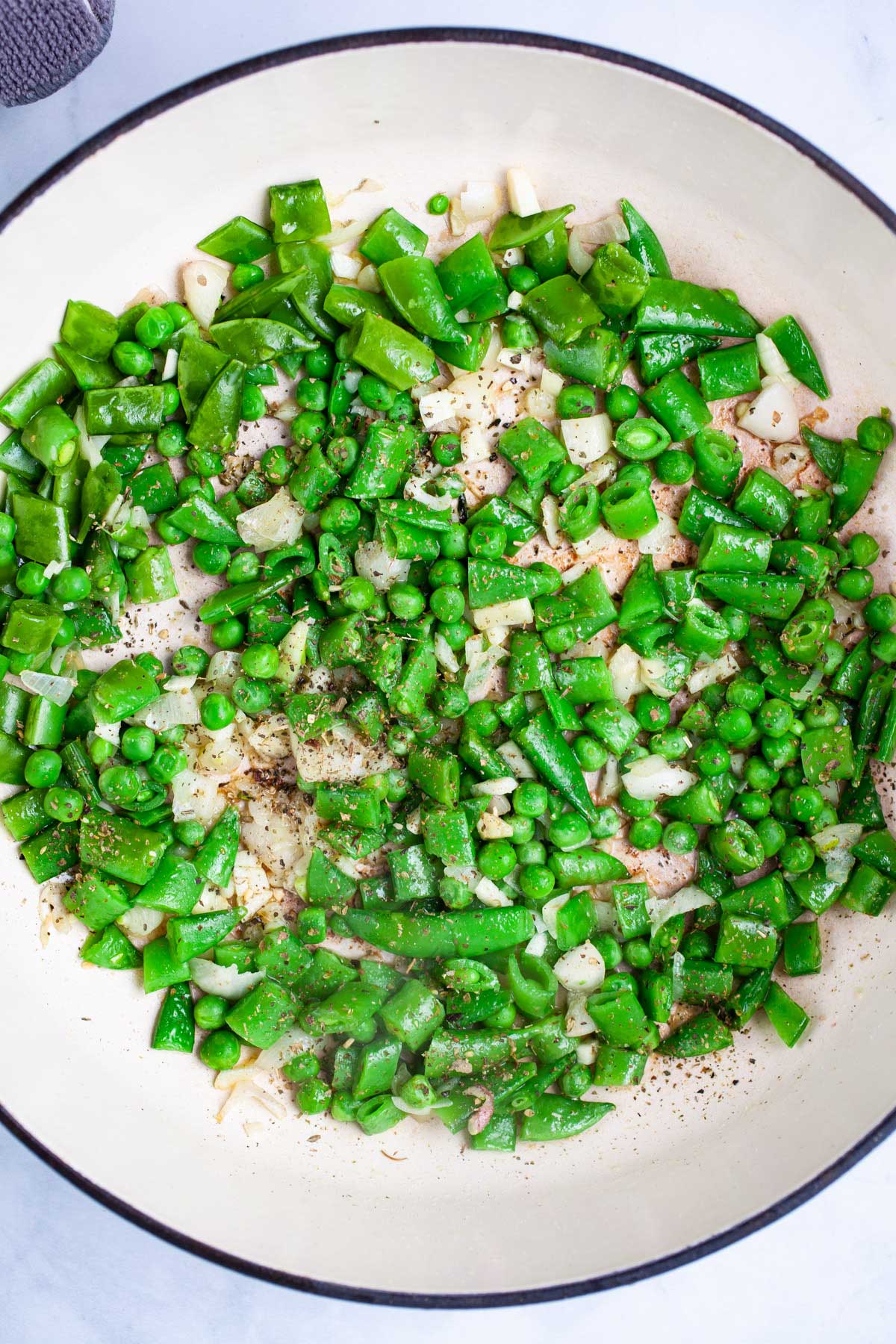 Peas, sugar peas, onions, and garlic, sauteed in olive oil in a pan.