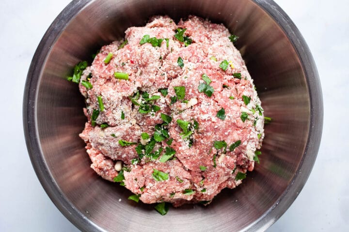 Parsley and cheese seasoned ground beef in a stainless steel bowl.