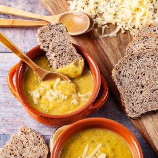 Two bowls filled with yellow squash soup, topped with Parmesan cheese and served with extra cheese and bread on the side.