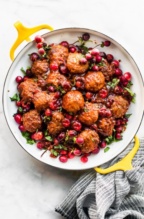 an overhead shot of cranberry chicken meatballs on a white plate with cooked whole cranberries nestled throughout.