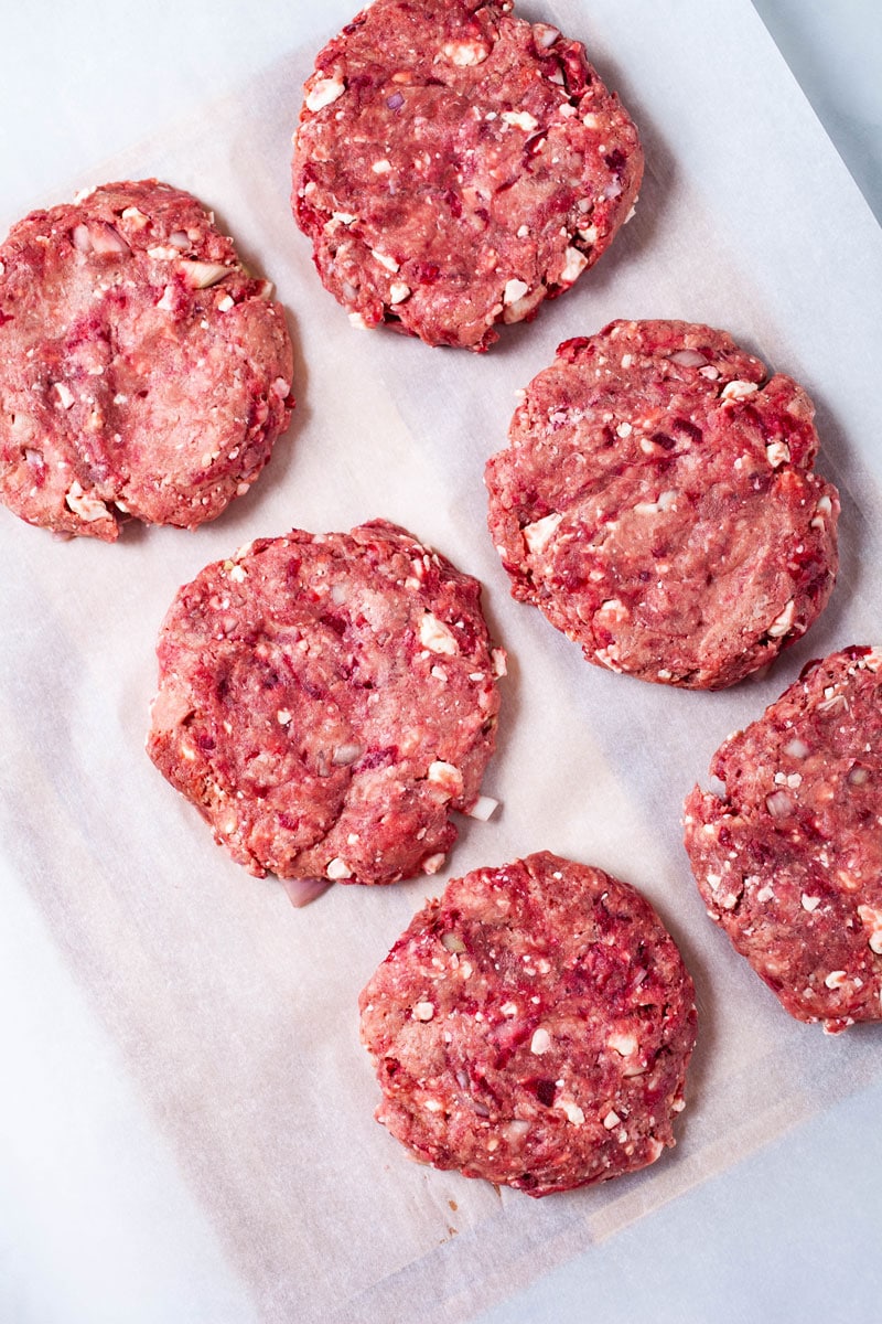 Raw seasoned hamburger patties on parchment paper.