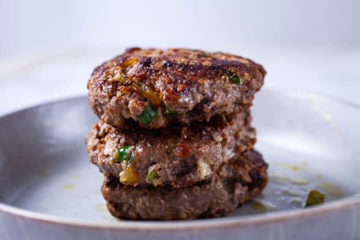 Three juicy cooked burgers stacked on top of each other, served on a plate.