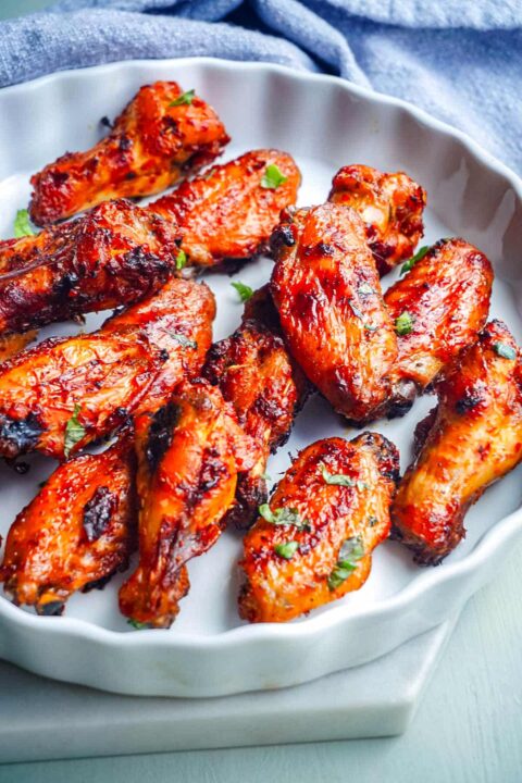harissa chicken wings garnished with some fresh herbs in a white pie plate with a blue towel in the background.