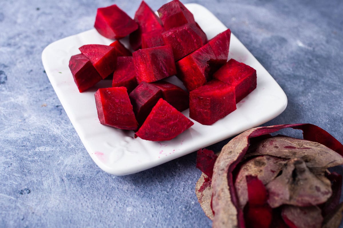 Peeled an chopped fresh red beets on a plate next to its peel.