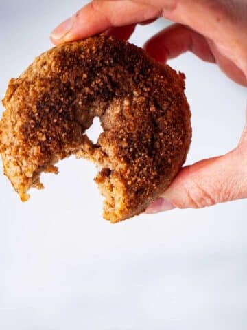 A close-up of a hand holding up a cinnamon sugar topped doughnut with a bite in it.