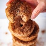 A close-up of a hand holding up a cinnamon sugar topped donut with a bite in it.