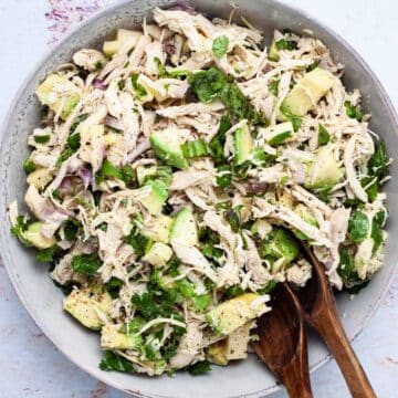 Two wooden spoons resting in a large plate filled with a healthy chicken salad with olive oil.