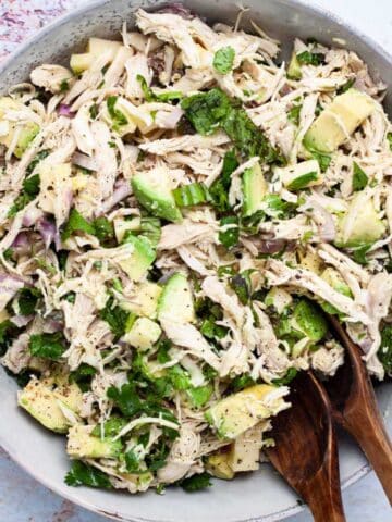 Two wooden spoons resting in a large plate filled with a healthy chicken salad with olive oil.