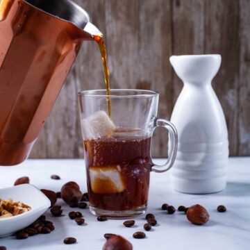 Someone pouring cold brew coffee concentrate in a tall glass filled with ice cubes.