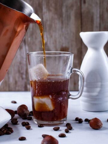 Someone pouring cold brew coffee concentrate in a tall glass filled with ice cubes.