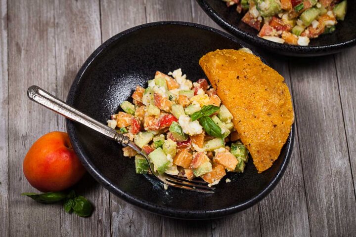 A bowl filled with a healthy egg salad and apricots with a taco on the side and a fork.