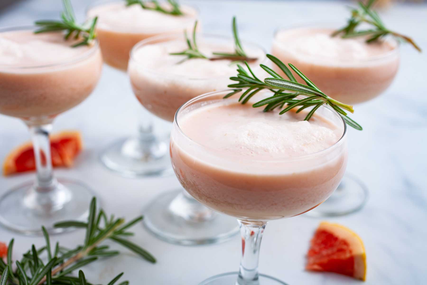 Festive grapefruit mocktails topped with Rosemary leaves served on a table.