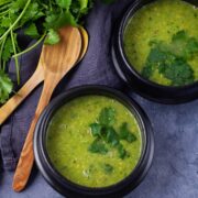 Two black bowls filled with green pea soup, topped with fresh Parsley leaves next to two wooden spoons and more fresh Parsley.