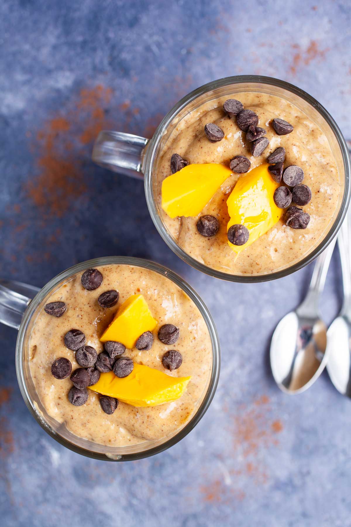 Two creamy chocolate mango smoothies topped with chocolate chips and fresh mango slices.