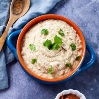 A terra cotta bowl filled with creamy mashed cauliflower and garnished with Parsley.