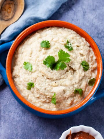 A terra cotta bowl filled with creamy mashed cauliflower and garnished with Parsley.