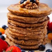 Oat flour pancakes stacked on top of each other and topped with maple syrup, nuts, and berries.