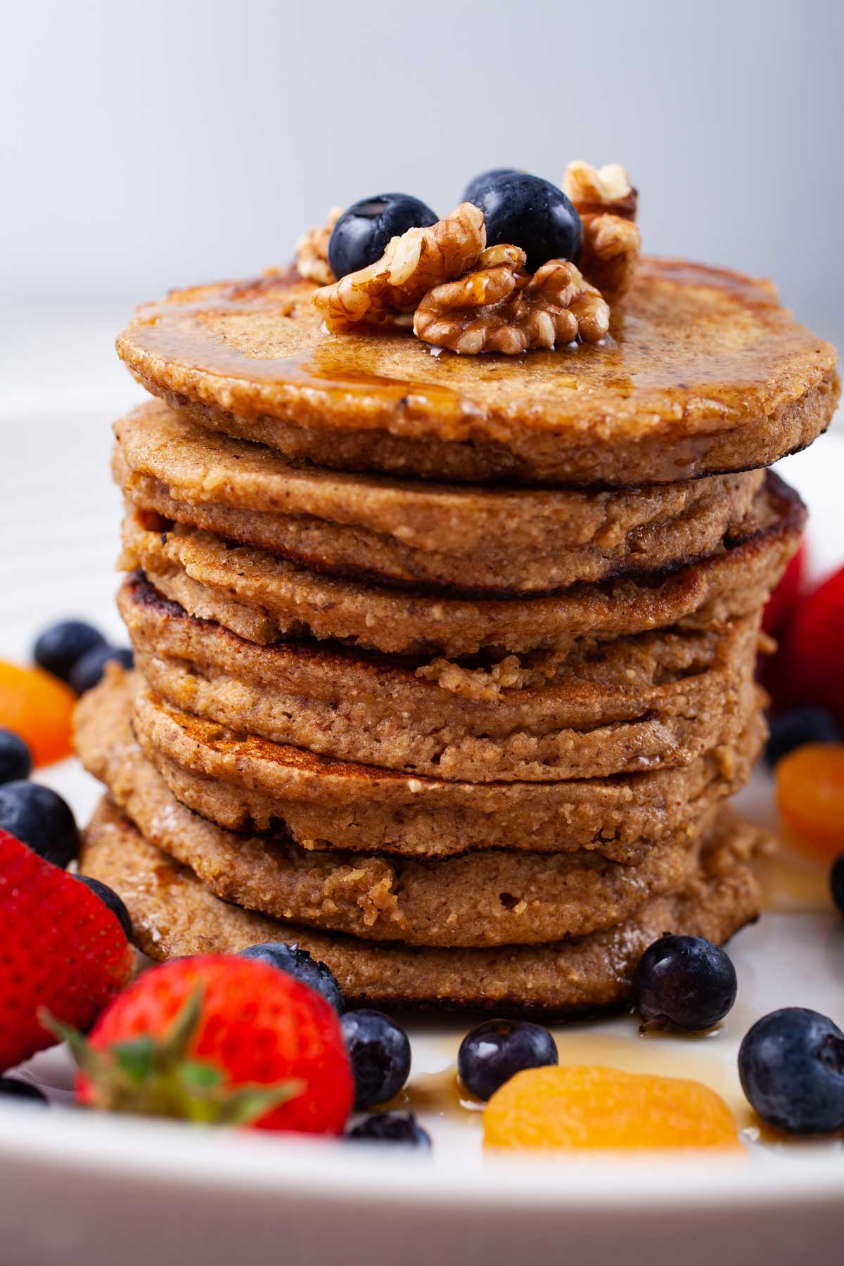 Oat flour pancakes stacked on top of each other and topped with maple syrup, nuts, and berries.