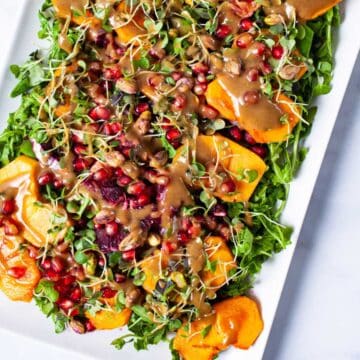 Persimmon arugula salad with a tahini dressing served on a large plate.