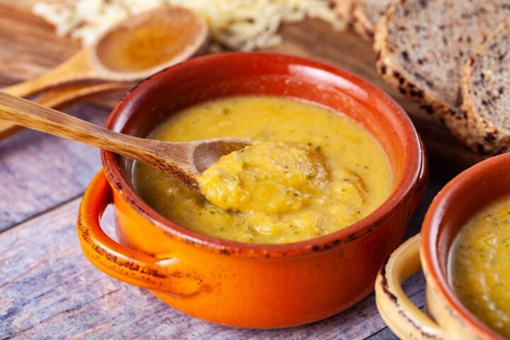 A wooden spoon dunked in a small terra cotta bowl filled with yellow squash soup.