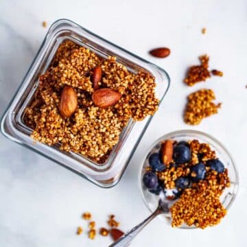 Golden brown clusters of steel-cut oats granola in a jar next to a small granola bowl with berries.