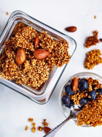 Golden brown clusters of steel-cut oats granola in a jar next to a small granola bowl with berries.