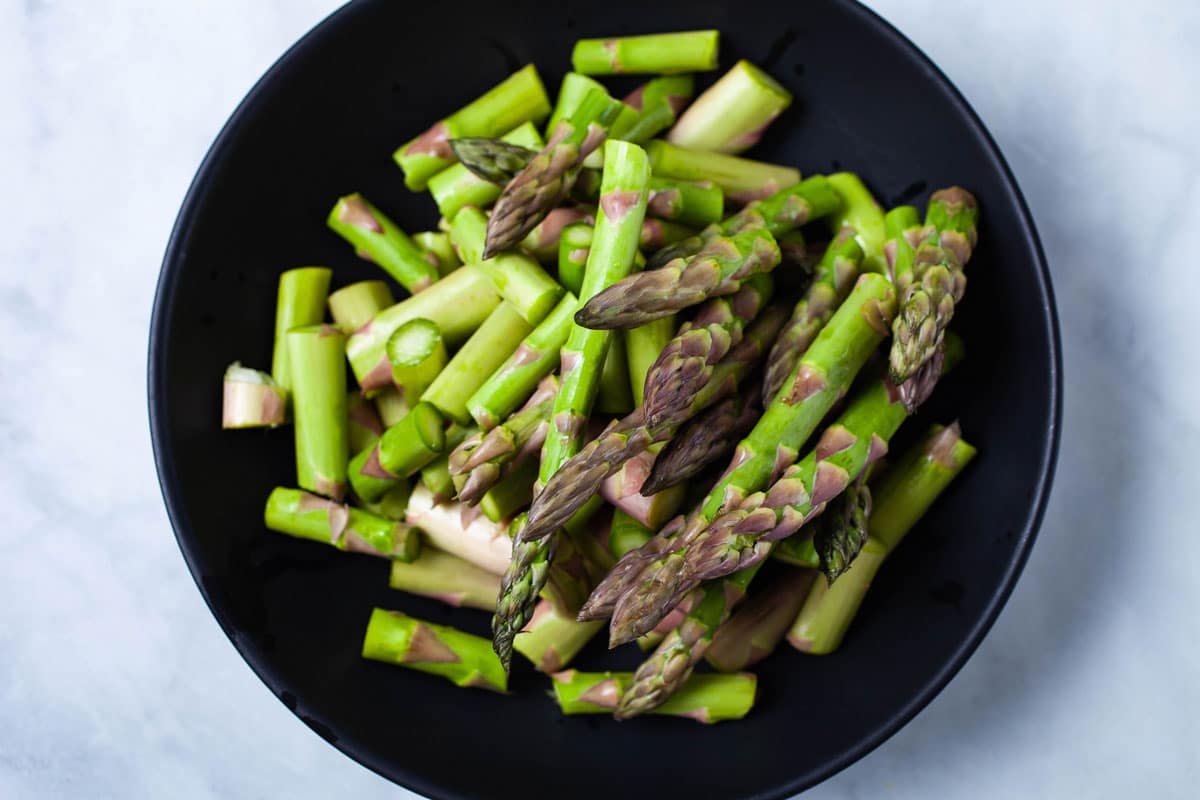 Chopped fresh asparagus in a black plate.