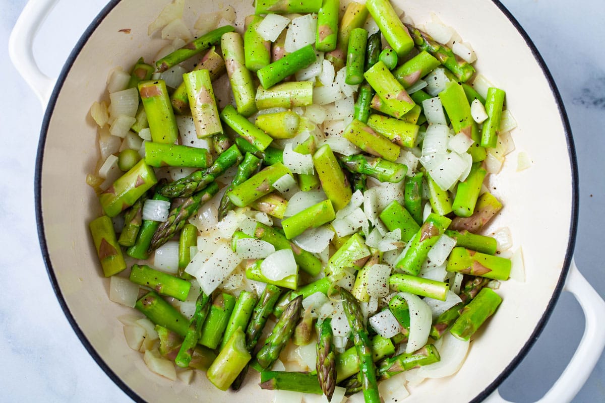 Chopped seasoned asparagus and onions in a large Dutch pan.