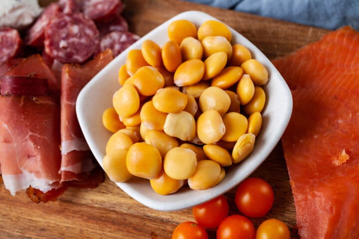 een close-up van een kleine kom met bereide Lupinibonen op een charcuterie bord.