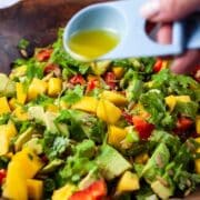 Someone pouring olive oil over a mango avocado salad.
