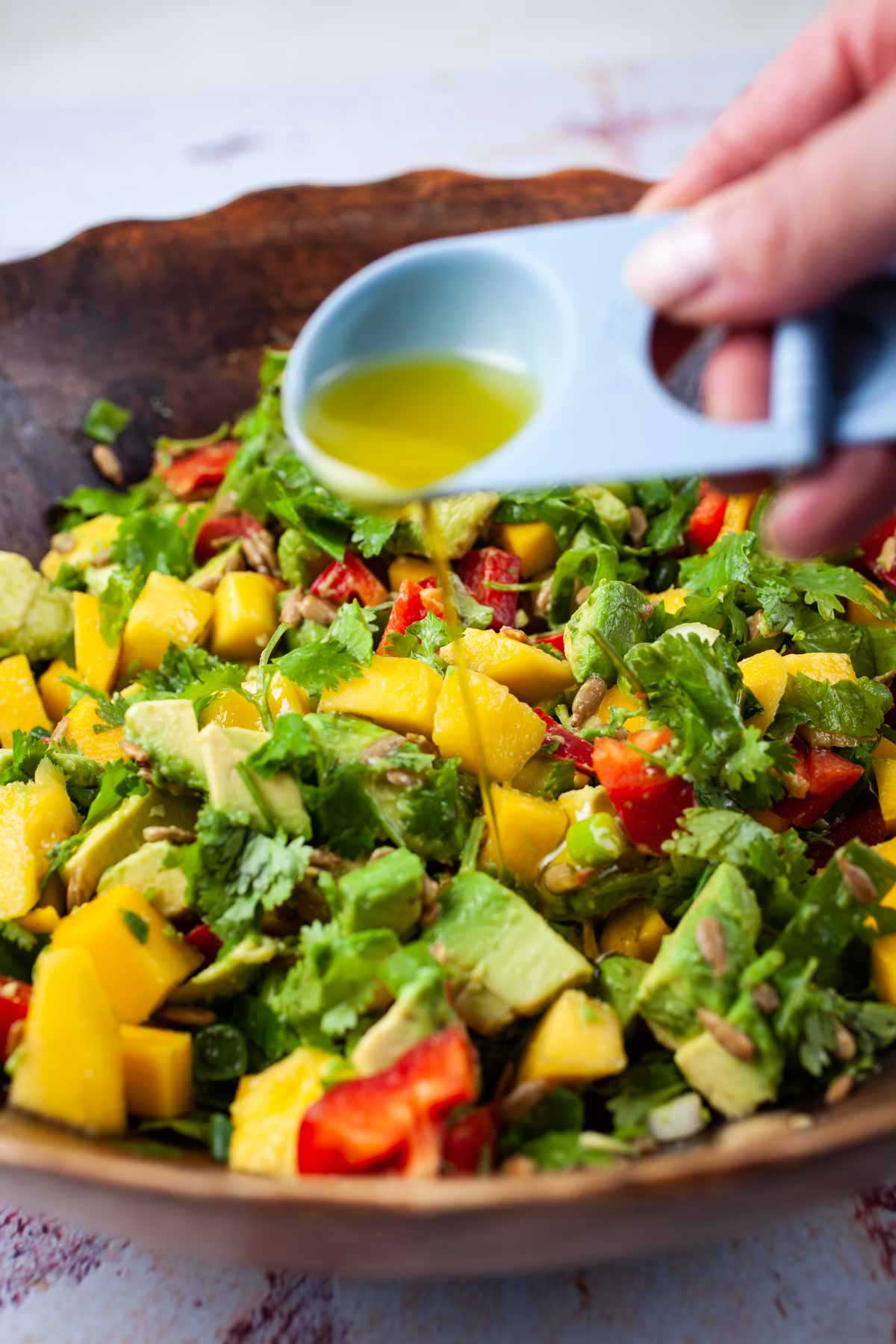 Someone pouring olive oil over a mango avocado salad.