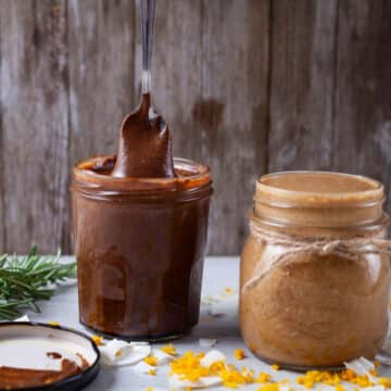 A small spoon lifting creamy chocolate nut butter out of a jar and next to another jar with coconut butter.